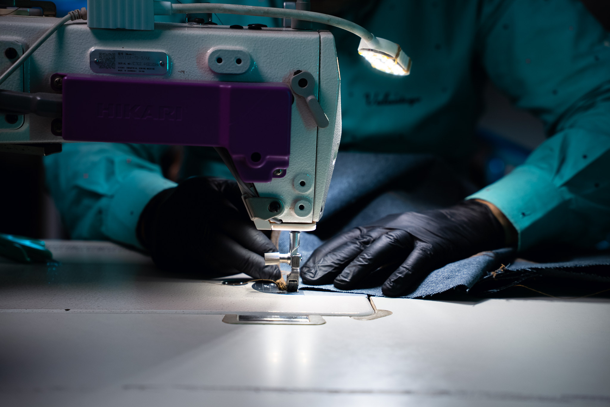 At the machine: gloved hands guide raw denim under the presser foot.
